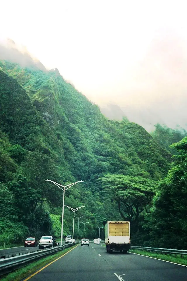 Cars and a truck driving on a mountain highway in Hawaiʻi with lush green hills
